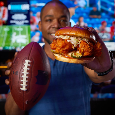 Man holding chicken sandwich and football.