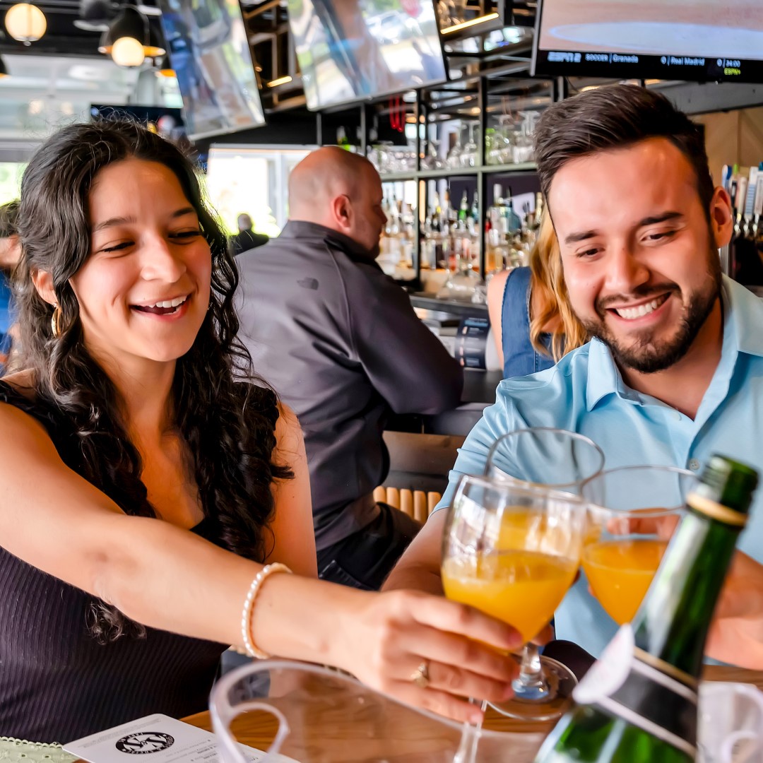 Couple toasting mimosas at Sports & Social restaurant.